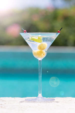 Glass of dry martini cocktail with sunlight bokeh on the pool nosing at the tropical resort. Verticalの写真素材