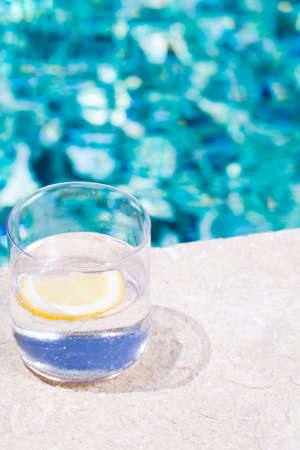 Glass of sparkling water with lemon on the pool nosing at the tropical resort. Vertical, glass on the left sideの写真素材