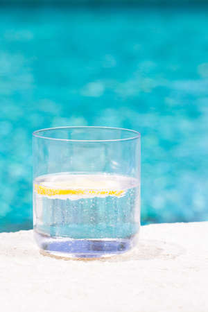 Glass of sparkling water with lemon on the pool nosing at the tropical resort. Vertical, glass on...