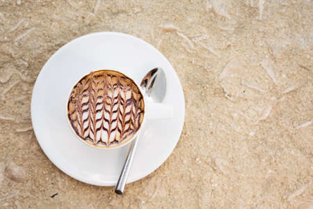 Overhead view of cafe latte with topping on it. Standing on sand. Horizontal. Top view