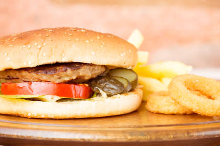 Classic homemade hamburger with onion rings and french fries on a wooden plate. Juicy homemade food. Horizontal, burger is croppedの写真素材