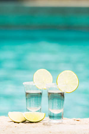 Two tequila shots with sliced lime on the beach. Transparent alcohol. Hanging out. Verticalの写真素材