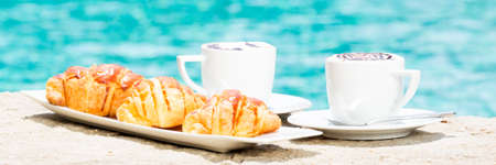 Side view of cafe latte with topping on it. Standing on sand with croissants on white plate. Horizontal, bannerの写真素材