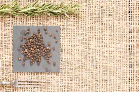 Black peppercorns on dark plate with rosemary and antique fork. Rustic background. Warm color. With copy space Horizontalの写真素材