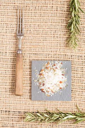 Salt with spices on dark plate with rosemary and antique fork. Rustic background. Warm color. Verticalの写真素材