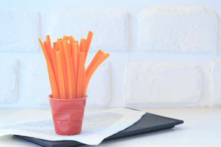 Carrot slices in a red porcelain glass. Healthy snack. Fresh high key veggie photo. Black background with white napkin. Horizontalの写真素材