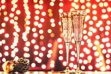 Two glasses of champagne with Christmas toys. Festive lights bokeh Christmas background. New Year holidays celebration. Horizontal, toned, rich redの写真素材