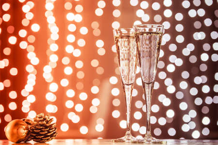 Two glasses of champagne with Christmas toys. Festive lights bokeh Christmas background. New Year holidays celebration. Horizontal, toned, red to dark brownの写真素材