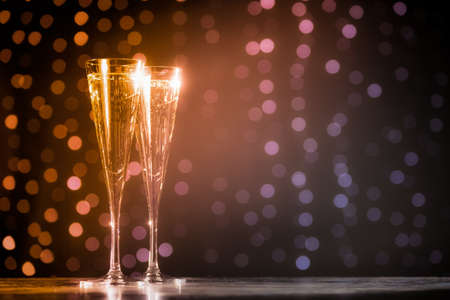Two glasses of champagne on dark bokeh background. Holiday concept. Festive bokeh background. Horizontal, toned, warm tone, orange to pinkの写真素材