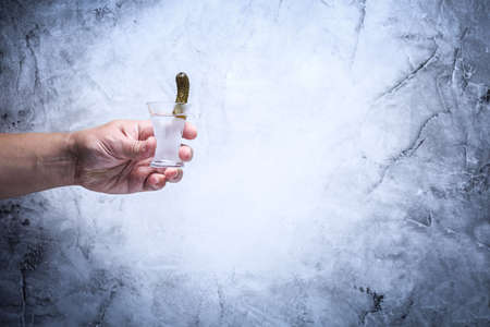 Drink responsibly!  Adult hand with shot of vodka. Grey background. Horizontal