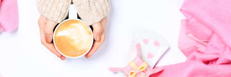 Female hands in beige knit holding cup of cappuccino. Gift alike dessert with heart shape sprinkles. Flat lay. Valentines concept. Pink textile. Horizontal, banner formatの写真素材