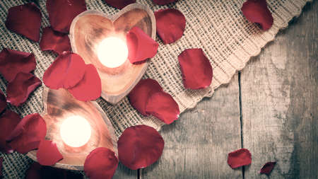 Enlightened candles in heart-shaped candle holders with red roses petals on rustic wooden background.の写真素材
