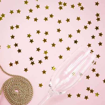 Festive evening golden clutch and champagne glass with star sprinkles on pink. Holiday and celebration background. Luxury accessories and party concept. Squareの写真素材
