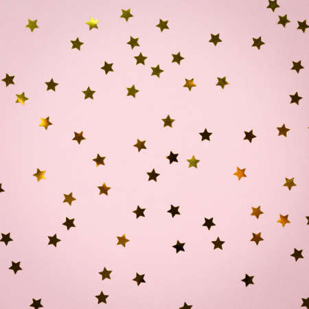 Golden star sprinkles on pink. Festive holiday background. Celebration concept. Top view, flat lay. Squareの写真素材