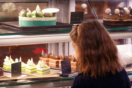 Little girl in confectionary shop looking at the display. Sweet treats variety. Small business and child concept. Horizontal Warm white balanceの写真素材