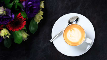 Coffee cup with latte art and flower bouquet. Concept of business event refreshment break. Top view. Black background. Horizontal, wide screen formatの写真素材