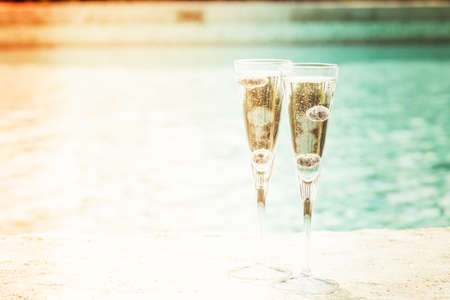 Two glasses of prosecco  cocktail with blueberries at the edge of a resort pool. Concept of luxury vacation. Outdoor pool background. Overlight toned image. Horizontalの写真素材