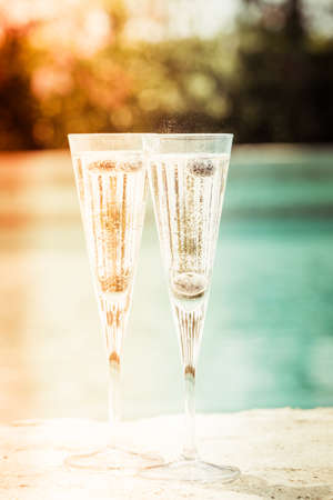 Two glasses of prosecco  cocktail with blueberries at the edge of a resort pool. Concept of luxury vacation. Outdoor pool background. Overlight toned image. Verticalの写真素材