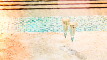 Two glasses of prosecco   at the edge of a resort pool. Concept of luxury vacation. Outdoor pool background. Overlight toned image. Horizontal, wide screen formatの写真素材
