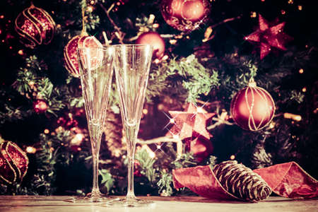 Two empty glasses  with Christmas tree background. Holiday season background. Traditional red and green Christmas decoration with lights. Holiday party. Horizontal, with sparkles and tonedの写真素材