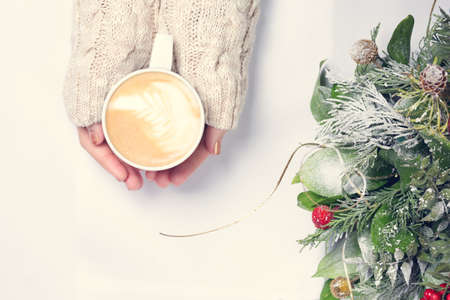 Girl holding cup of coffee with latte art. Christmas background. Hygge and leasure time concept. Pastel colors, warm toning. Horizontalの写真素材