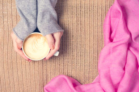 Girl holding cup of coffee with latte art. Pink textile. Leisure time concept. Pastel colors, warm toning. Horizontalの写真素材