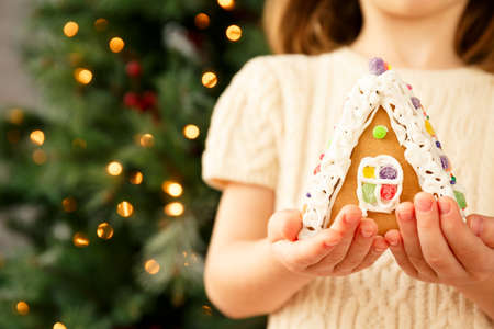 Girl holding a gingerbread house with Christmas tree background. Holiday concept. Horizontalの写真素材