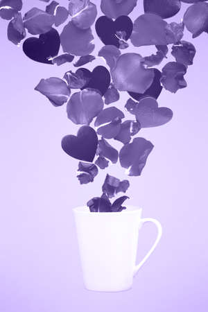 Levitating coffee mug with splashes of rose petals and hearts. Surprise, holiday and coffee love concept. Minimal art trend. Solid background. Vertical, ultra violet tone, color of the yearの写真素材