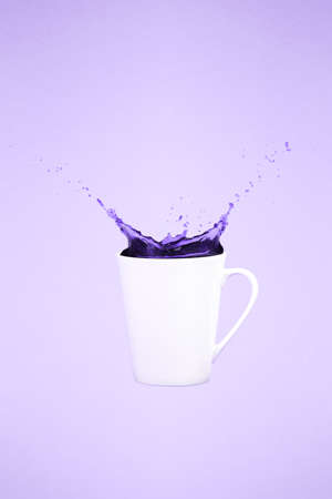 Levitating coffee mug with splashes. Coffee concept. Minimal art trend. Solid background. Vertical, straight cup, ultra violet tone, color of the yearの写真素材