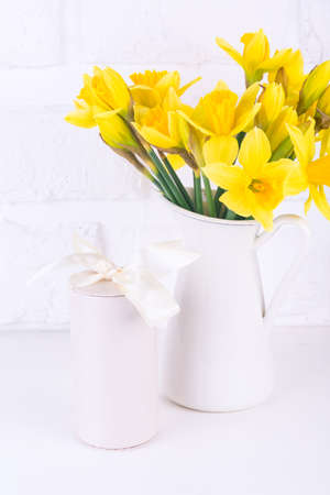 Jar with narcissuses and a gift box at the white background. Vertical Spring, mothers day and easter conceptの写真素材