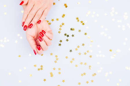 Woman hand with red manicure on blue background with sprinkles. Holiday, party and celebration concept. Horizontalの写真素材