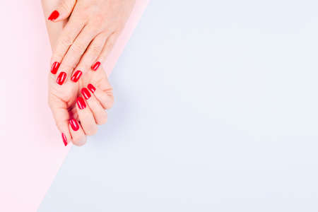 Woman hands with stylish red manicure on pastel blue and pink background. Holiday, party and beauty concept. Horizontalの写真素材