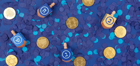 Dark blue background with multicolor dreidels and chocolate coins on blue confetti. Hanukkah and...