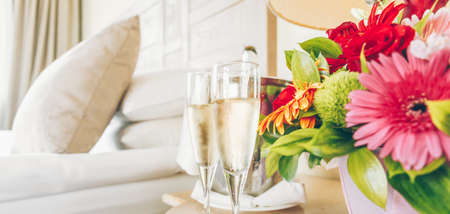 Two glasses of champagne in the upscale hotel room. Dating, romance, honeymoon, valentine, getaway concepts. Horizontal, banner wide screen format. Light warm toningの写真素材