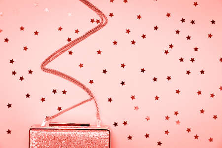 Festive evening golden clutch with star sprinkles on pink. Holiday and celebration background. Luxury accessories and party concept. Horizontal. Living coral theme - color of the year 2019の写真素材