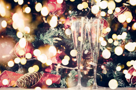 Two glasses of champagne with Christmas tree background. Holiday season background. Traditional red and green Christmas decoration with lights. Holiday party. Horizontal, toned, with sparkles and toned. Festive bold bokehの写真素材
