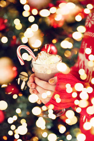 Girl holding cacao with whipped cream and peppermint candy cane. Christmas holiday concept. Holiday background. Holiday or winter background. Vertical Vertical. Festive bold bokehの写真素材