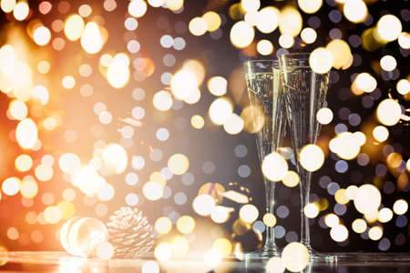 Two glasses of champagne with Christmas toys. Festive lights bokeh Christmas background. New Year holidays celebration. Horizontal, toned, orange to lilac, bold light bokehの写真素材