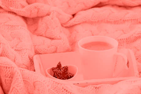 Hot beverage mug with chocolate cookies in a white wool blanket. Hot drink, cozy home and cold season concept. Horizontal. Coral accent - color of the year 2019の写真素材