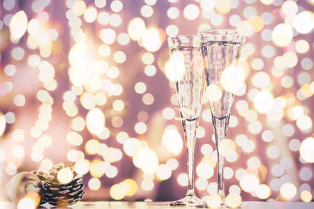 Two glasses of champagne with Christmas toys. Festive lights bokeh Christmas background. New Year holidays celebration. Horizontal, toned, delicate lilac, bold light bokehの写真素材