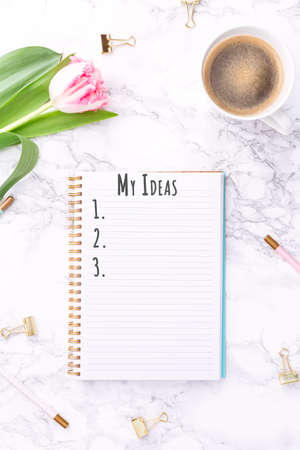 Pink tulips with festive stationary and coffee on white marble background. My Ideas wording. Copy space Top view. Verticalの写真素材