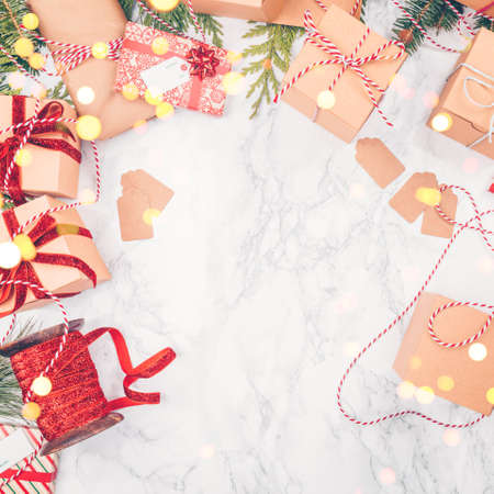 Craft boxes and wraps packed as Christmas gifts and red ribbons on white marble background with festive bokeh lights. Holiday season concept. Square, place for textの写真素材