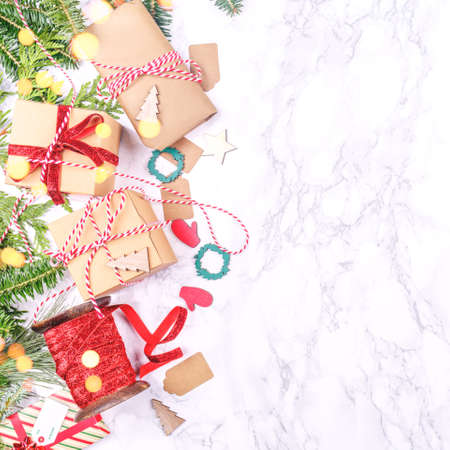 Craft boxes and wraps packed as Christmas gifts and red ribbons on white marble background with festive bokeh lights. Holiday season concept. Square, place for textの写真素材