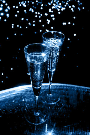 Two glasses of champagne on the glass table on black background, toned in blueの写真素材