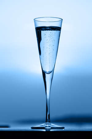 Glass of prosecco at a wooden pier at sunset. Luxury resort vacation concept. Festive relax getaway background toned on blue. Verticalの写真素材