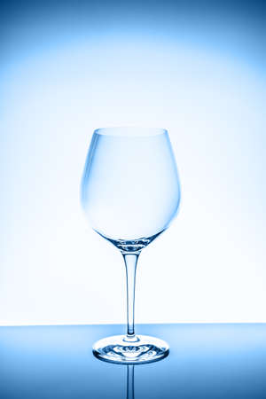 Red wine glass on the light background. Fine cristal glassware concept. Vertical, toned in blueの写真素材