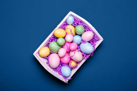 Multicolor eggs in a white tray. Creative Easter concept. Modern solid classic blue background. Horizontalの写真素材