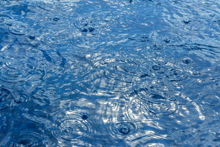 Blue water surface texture during rain. Monochrome classic blue background with place for text. Horizontal, soft focusの写真素材