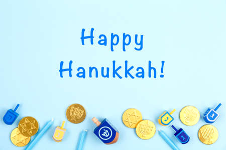 Blue background with multicolor dreidels, menora candles and chocolate coins and Happy Hanukkah wording. Hanukkah and judaic holiday concept. Horizontalの写真素材