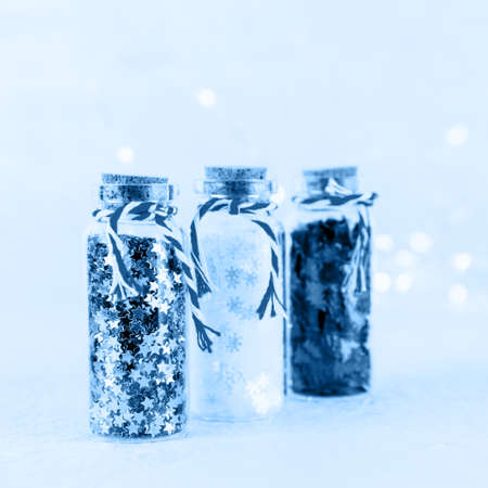 Glass bottles with glitter confetti on white background with bokeh lights. Holiday Christmas and New Year background toned in classic blue. Squareの写真素材